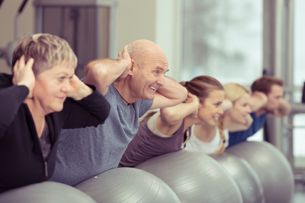 Happy elderly couple exercising in a pilates class at the gym with three other younger people toning and strengthening their muscles using gym balls, focus to the senior man and woman.jpeg